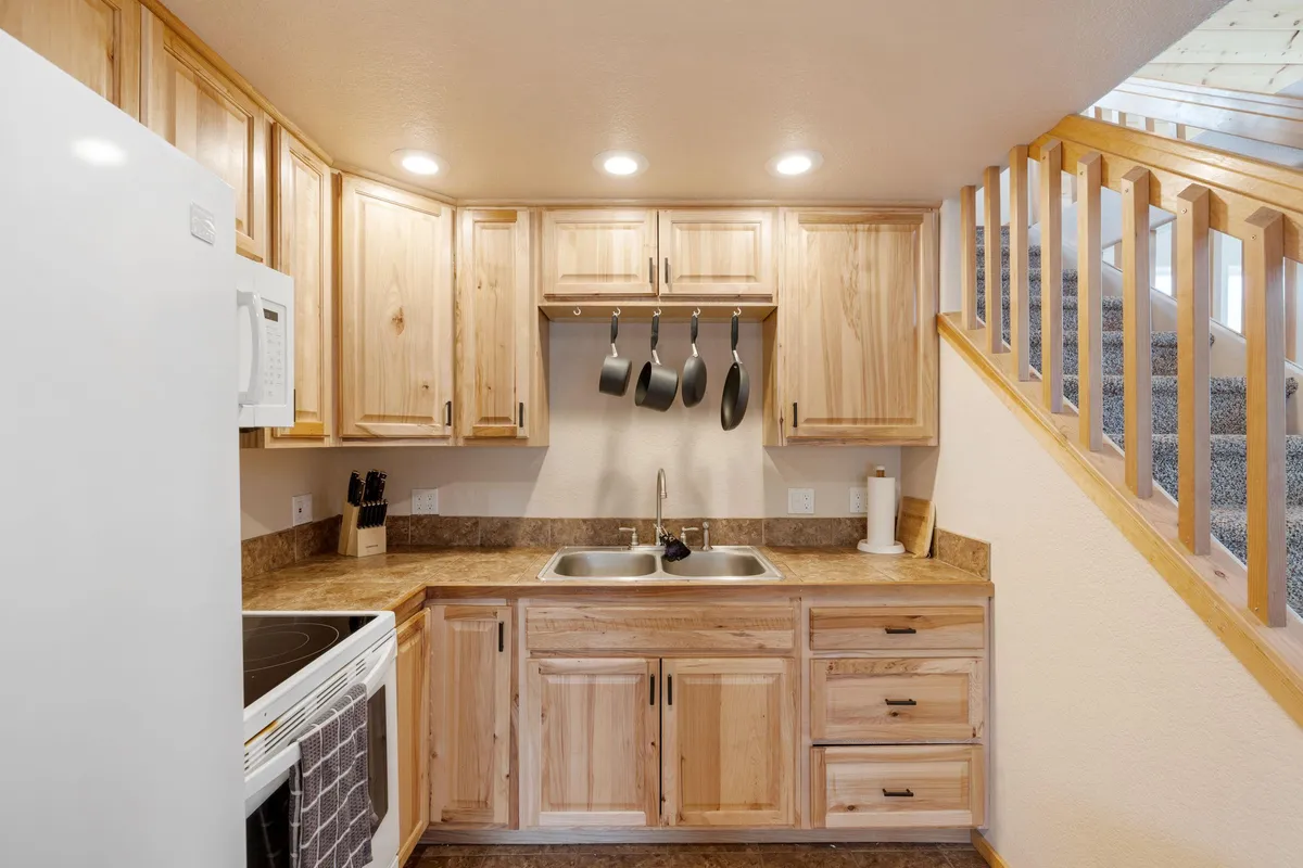 A cozy kitchen scene with a farmhouse sink, warm wooden cabinets, and hanging pots, inviting guests to cook, entertain, and share homemade meals. The kitchen is practical yet welcoming, reflecting the joy of shared culinary experiences.