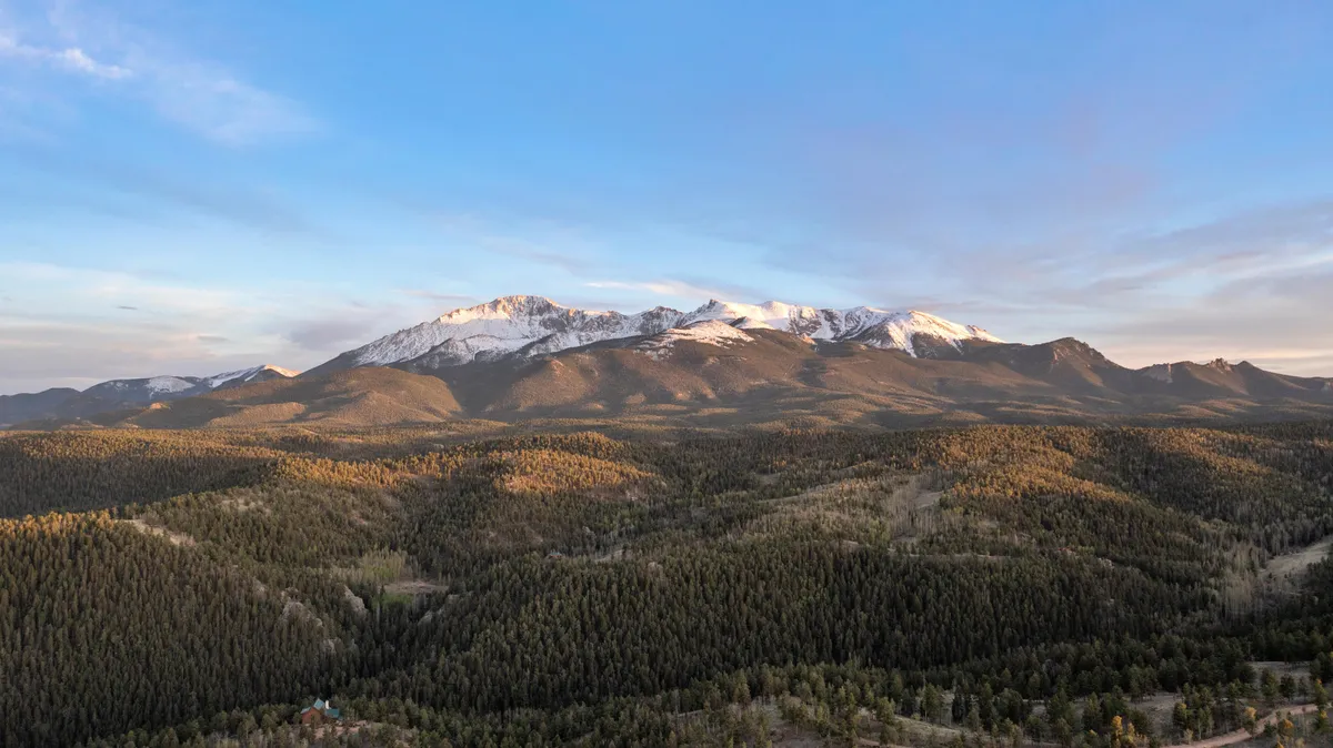 This image captures an expansive view of distant snow-capped mountains, rolling green forests, and softly undulating hills, evoking the wild, unspoiled beauty of the Colorado Rockies. The scene inspires a sense of adventure and is ideal for outdoor activities such as hiking, wildlife observation, or photography.