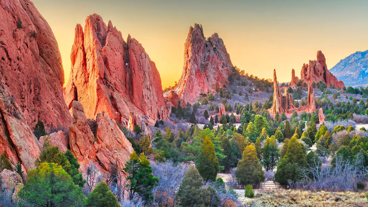 The view features majestic rock formations surrounded by dense evergreen trees beneath a vibrant sunset sky. The composition speaks to the serenity and beauty of the Colorado wilderness, inviting exploration and immersion in nature.