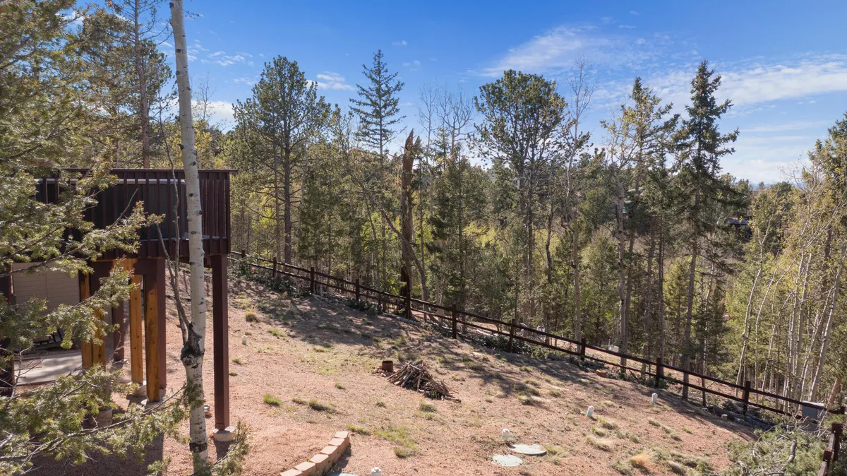 A serene exterior shot featuring tall trees surrounding a fenced patio area. The natural setting feels secluded, inviting guests to engage in nature walks or watch for local wildlife from a comfortable vantage point. The patio structure subtly suggests a place to relax and observe the environment.