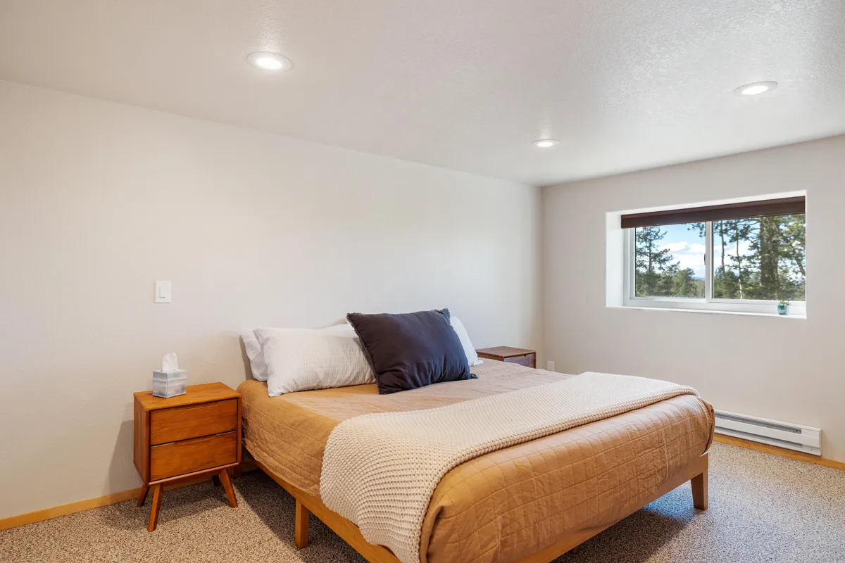 A tranquil bedroom featuring a comfortable bed, a window letting in soft natural light, and a nightstand for evening reading. The space is serene and welcoming, embodying the promise of privacy and restful moments away from the group.