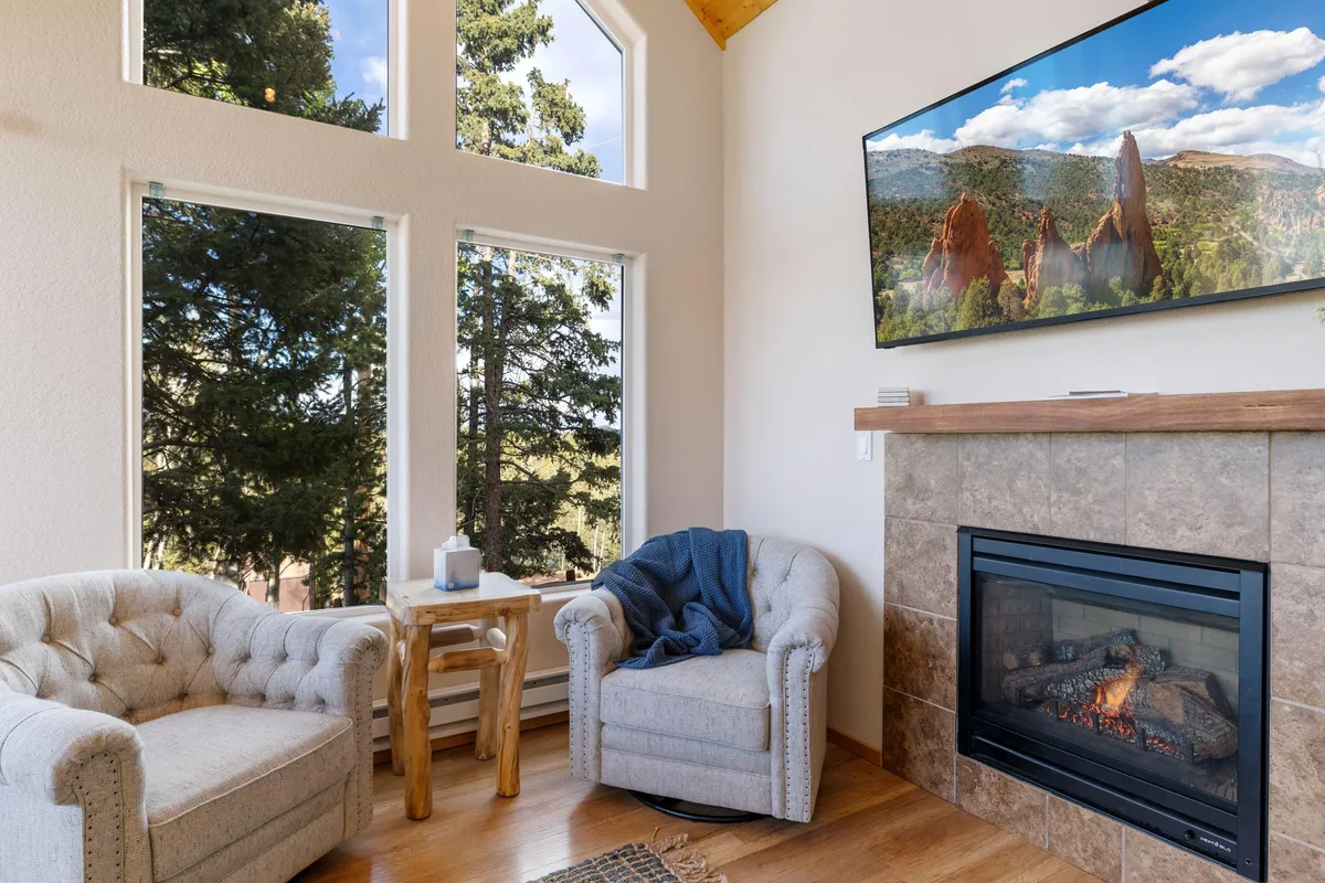 A cozy sitting area featuring comfortable armchairs, a modern fireplace, and floor-to-ceiling windows with views of the surrounding trees. The design encourages relaxation, conversation, and enjoying sunsets or stargazing from indoors.